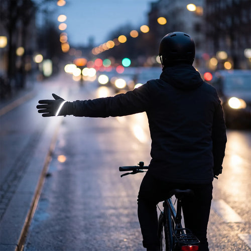 Radfahrer zeigt im Dunkeln das Handzeichen zum Abbiegen, der Reflektorstreifen am Dämmer-Handschuh leuchtet